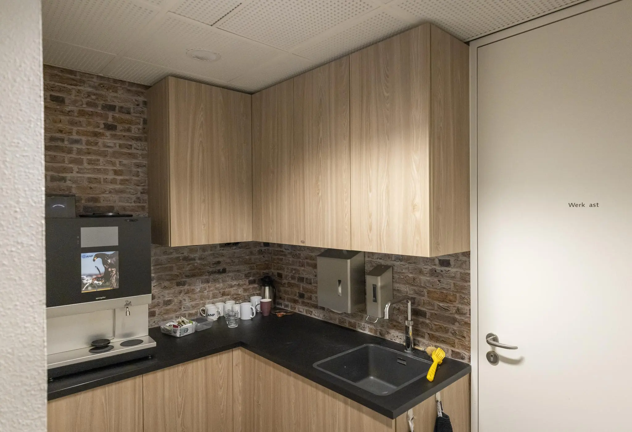 Kleine pantry met koffieautomaat, spoelbak en houten keukenkastjes in een kantoor aan de Prinses Beatrixlaan.